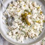 a spoon in a bowl of dill pickle chicken salad next to crackers and a jar of pickles