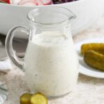 A jar of dill pickle salad dressing with pickles beside it
