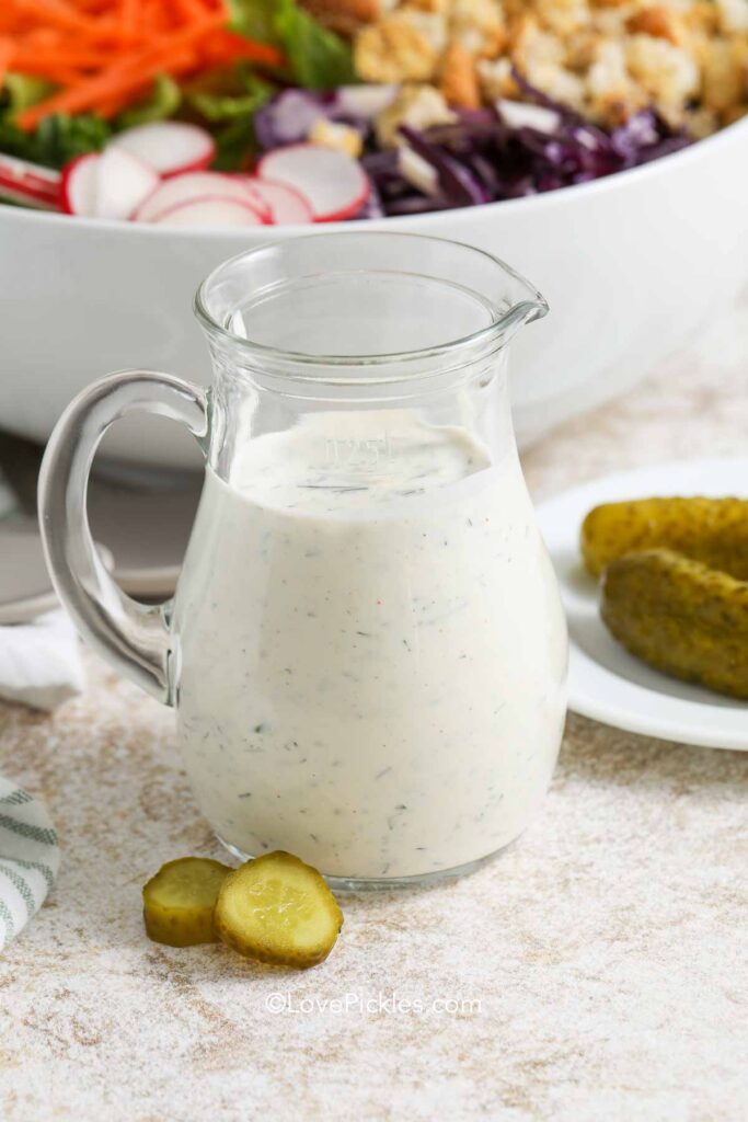 A jar of dill pickle salad dressing with pickles beside it
