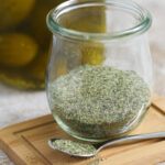 A jar of dill pickle seasoning on a small wood board