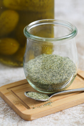 A jar of dill pickle seasoning on a small wood board