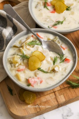 a bowl of Polish dill pickle soup with a spoon garnished with sprigs of dill and pickle slices