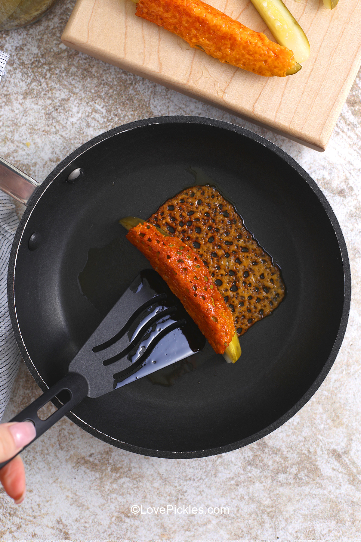 Using a spatula to roll up pickle in browned cheese to make chickles.