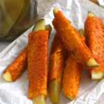 A plate of chickles with a jar of pickles in the background and a small bowl of ranch dressing.