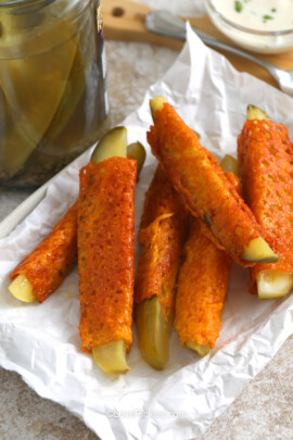 A plate of chickles with a jar of pickles in the background and a small bowl of ranch dressing.