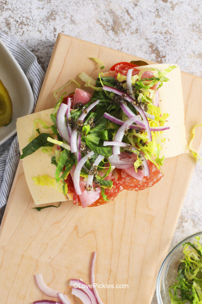 Adding lettuce, tomato, red onion and seasonings to pickle sandwich.