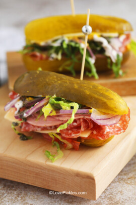 A fully assembled pickle sandwich with salami, cheese, lettuce, onion, and tomato, all sandwiched between the halves of a large pickle and held together with a sandwich pick.