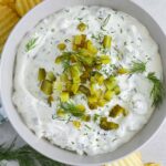 a bowl of dill pickle dip garnished with dill pickles and fresh dill