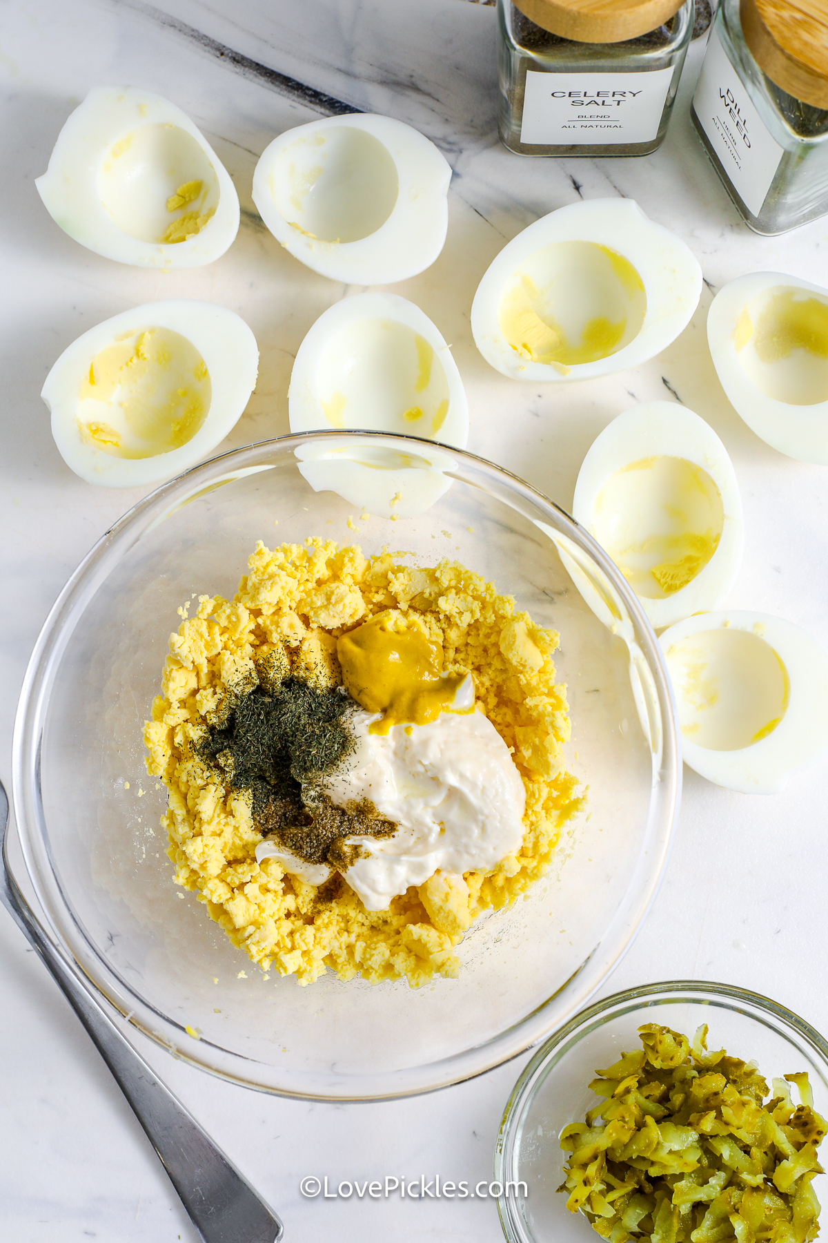 ingredients for dill pickle deviled eggs being mixed together in a bowl.