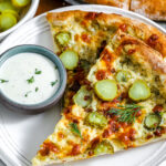Two slices of dill pickle pizza on a plate with dip on the side.