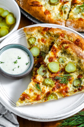Two slices of dill pickle pizza on a plate with dip on the side.