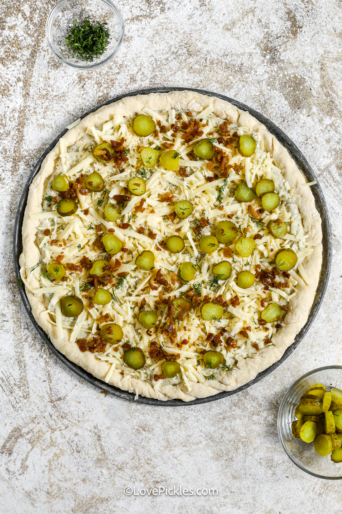 Dill pickle pizza is a tangy, cheesy dream! A creamy, herbal sauce is the perfect match for loads of cheese and layers of zesty dill pickles. Bacon bits add smoky crunch, while fresh dill makes every bite pop. It’s baked until golden and served hot and bubbly. The perfect food for a Friday night in or your next pizza party. Give this unique pie a try, you won’t regret it! #lovepickles Adding pickles and bacon bits to dill pickle pizza
