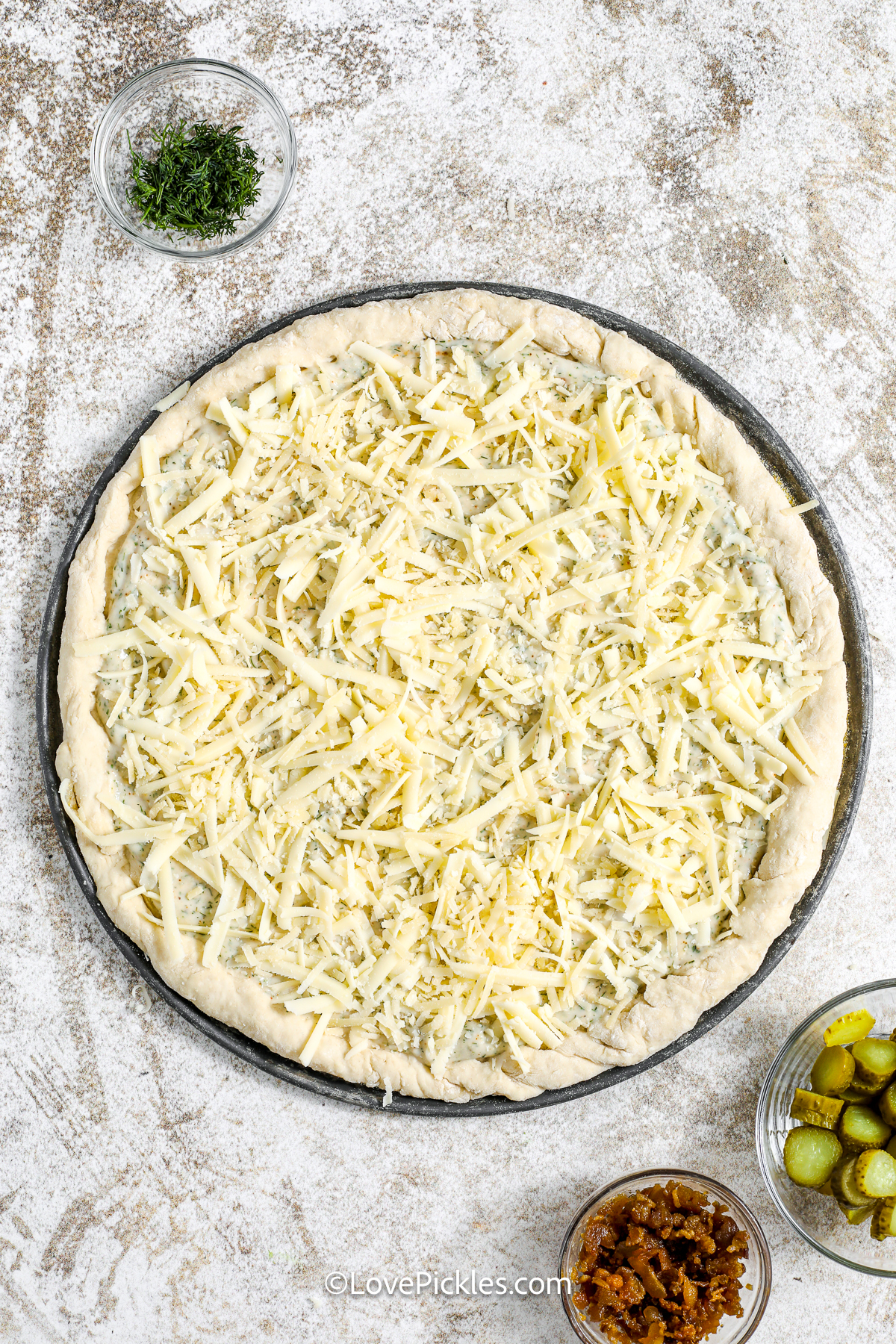 This dill pickle pizza is seriously next-level! The sauce is creamy with just the right kick of dill and spice, and it's topped with stretchy cheese, salty bacon, and tart pickle slices. Bake it up golden and finish with fresh dill for a fun, craveable twist on pizza night. It’s a bold and delicious way to shake things up in the kitchen! #lovepickles cheese added to pizza dough and sauce to make dill pickle pizza