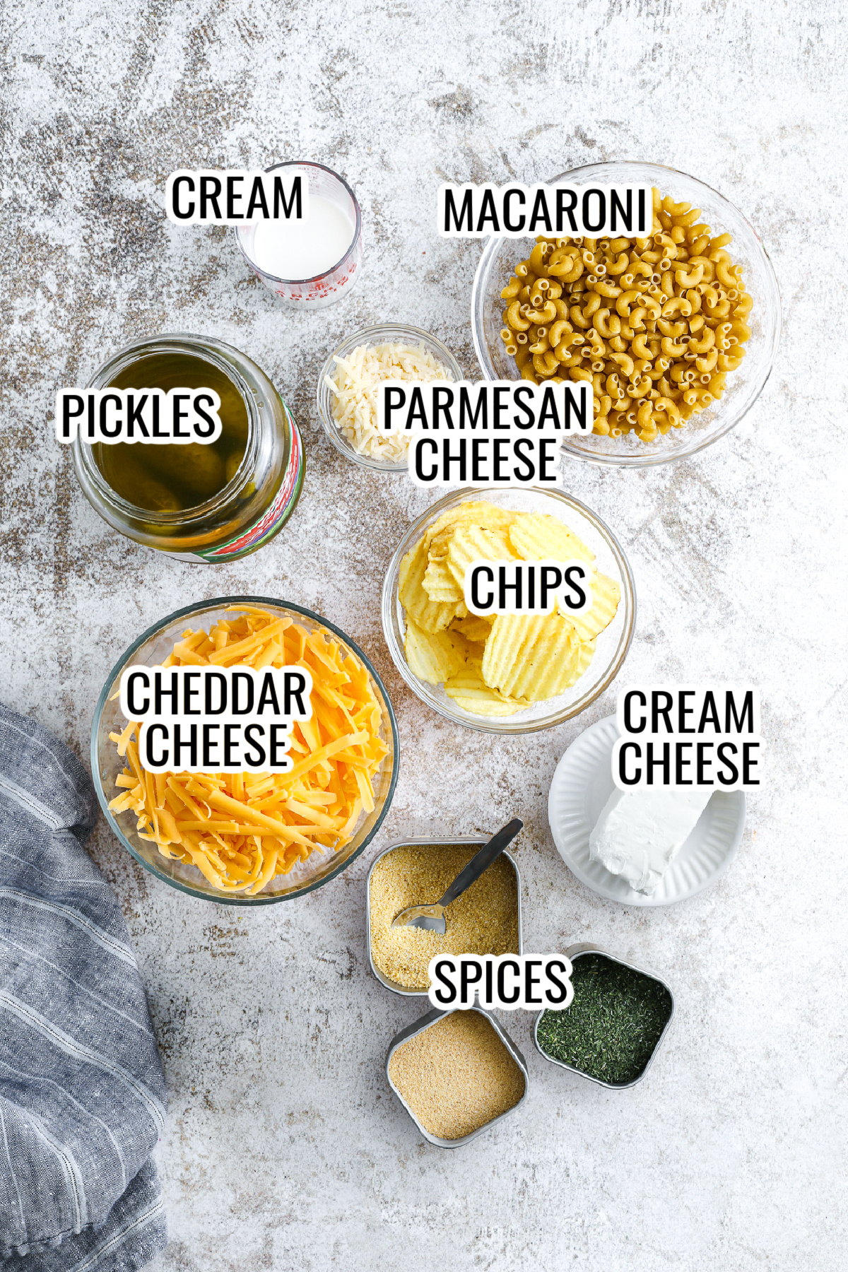 ingredients for dill pickle mac and cheese, including pickles, cheddar cheese, parmesan cheese, cream cheese, chips, macaroni, spices, and cream.