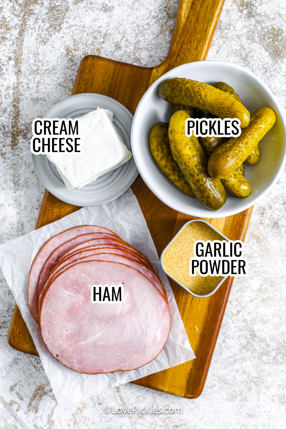 ingredients assembled to make dill pickle roll ups including cream cheese, pickles, ham, and garlic powder, with labels.