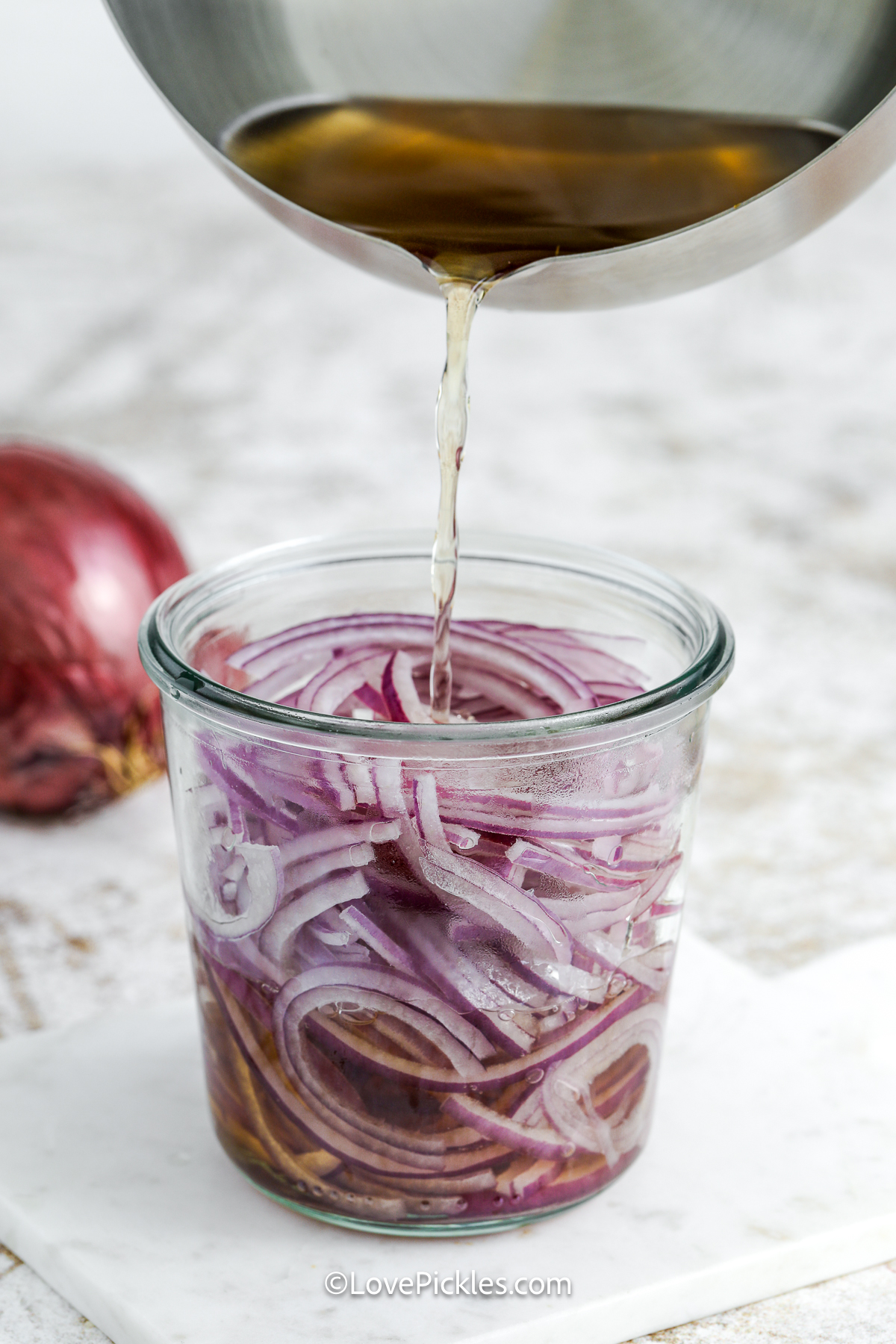 pouring brine into jar containing sliced red onions.