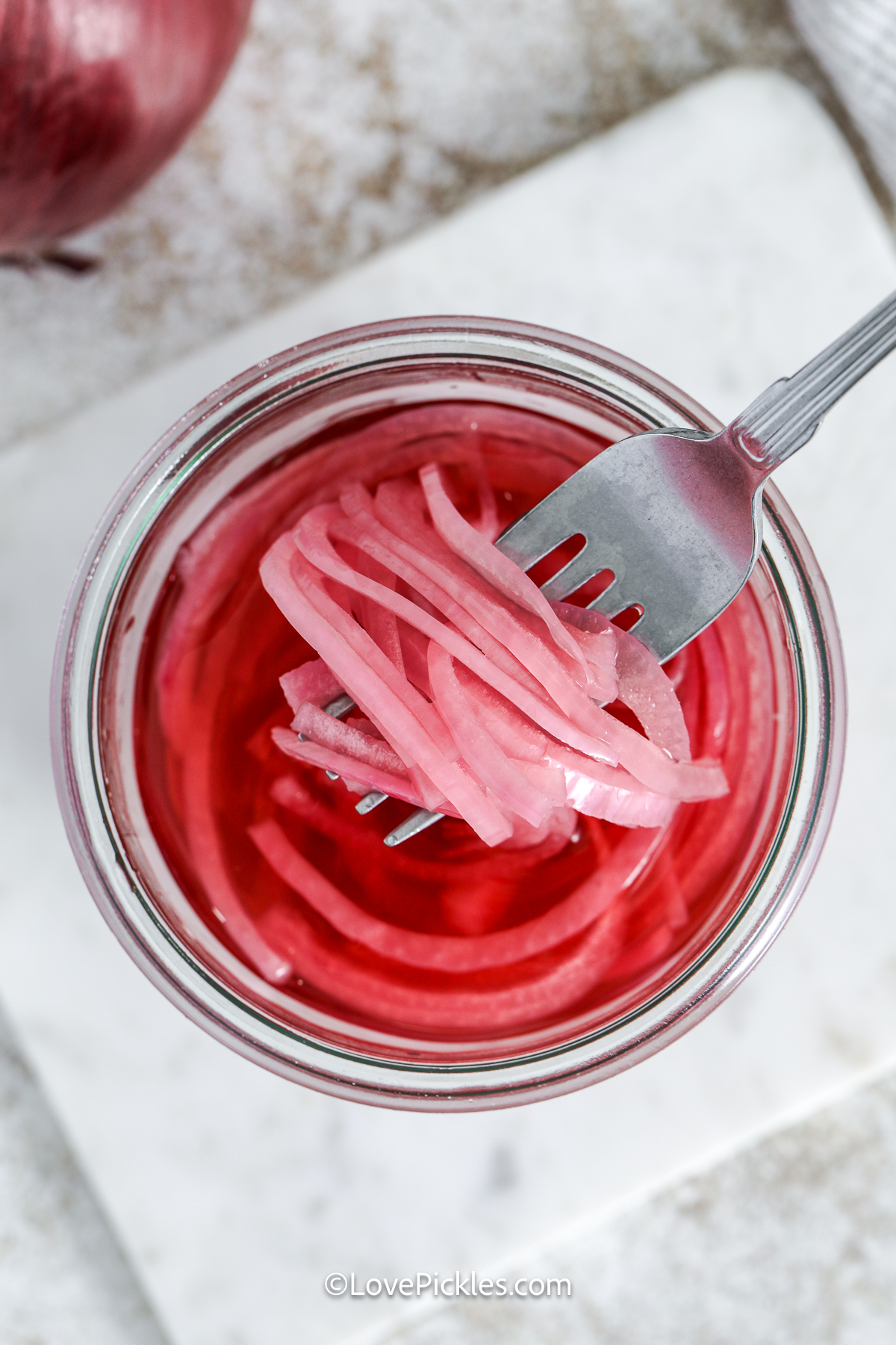 fork scooping pickled red onions from a jar.