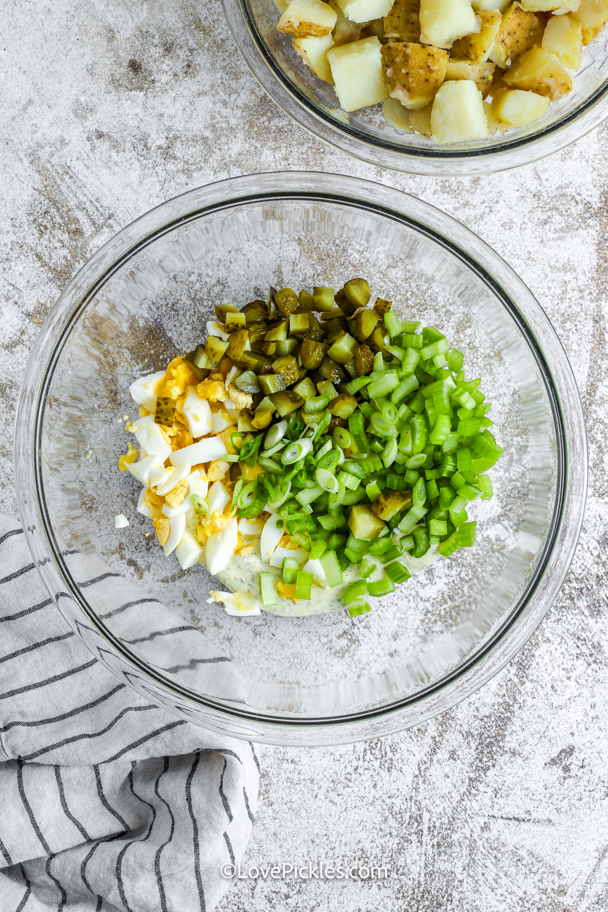 If you love pickles, you need to try this dill pickle potato salad! The potatoes are boiled until tender, then tossed with a punchy, creamy dressing made with mayo, pickle juice, and mustard. Celery, chopped pickles, and hard-boiled egg add flavor and crunch in every bite. This easy side dish is a summer must-have and totally make-ahead friendly too. #lovepickles Ingredients added to bowl for making dill pickle potato salad.