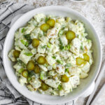 dill pickle potato salad in a bowl, with a bowl of pickles and salt& pepper.