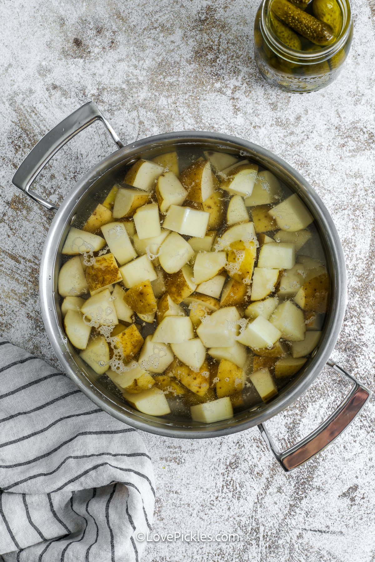 This easy dill pickle potato salad is the side dish your cookout needs! Tender potatoes are tossed with pickles, celery, and egg, then mixed in a zesty mayo dressing with mustard and dried dill. The flavor gets better as it chills, making it perfect to make ahead. Serve it cold with burgers, hot dogs, or grilled chicken—it’ll be gone in no time! #lovepickles chopped potatoes in a pot for dill pickle potato salad.