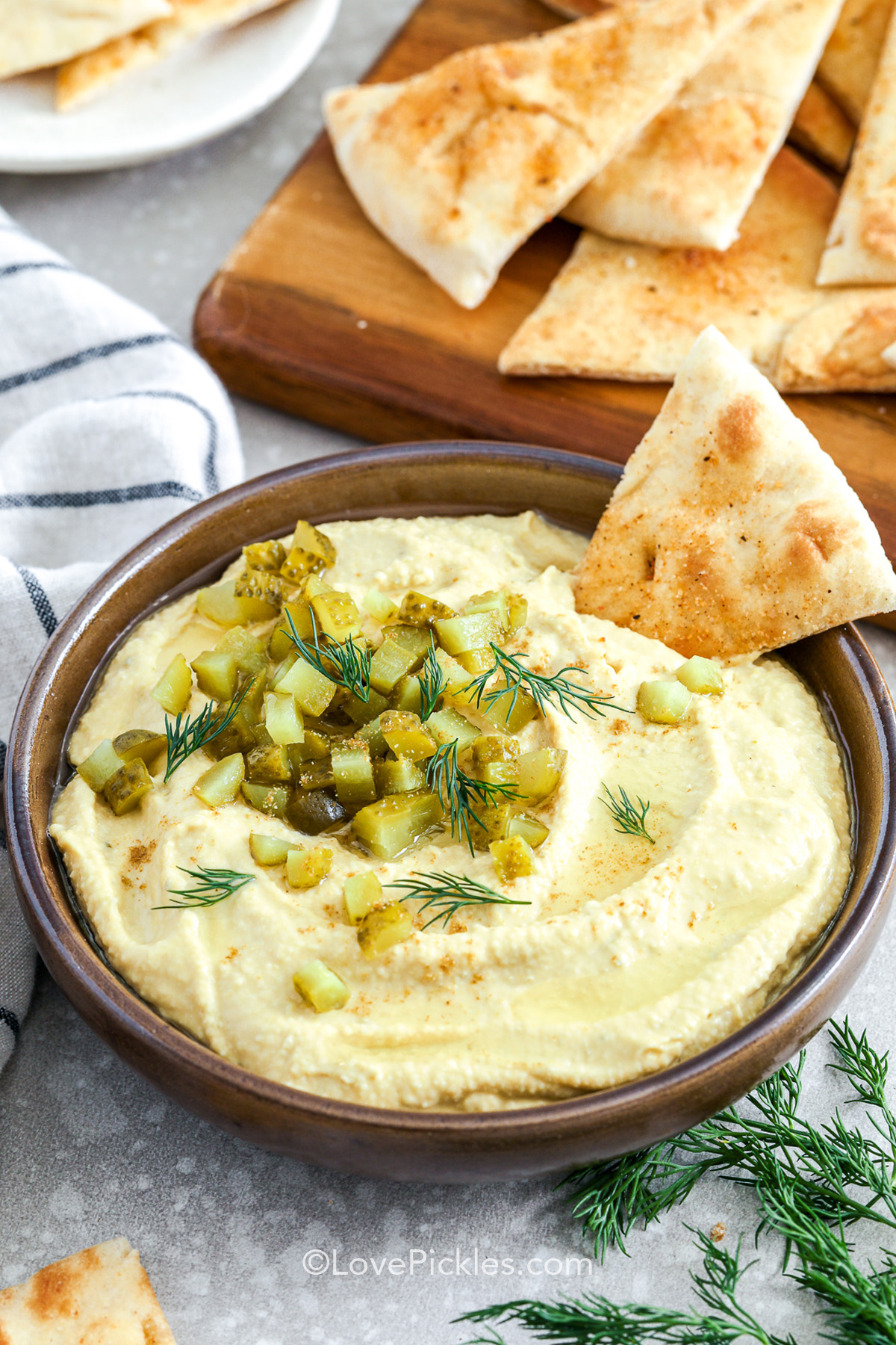 dill pickle hummus in a bowl with a garnish of pickles