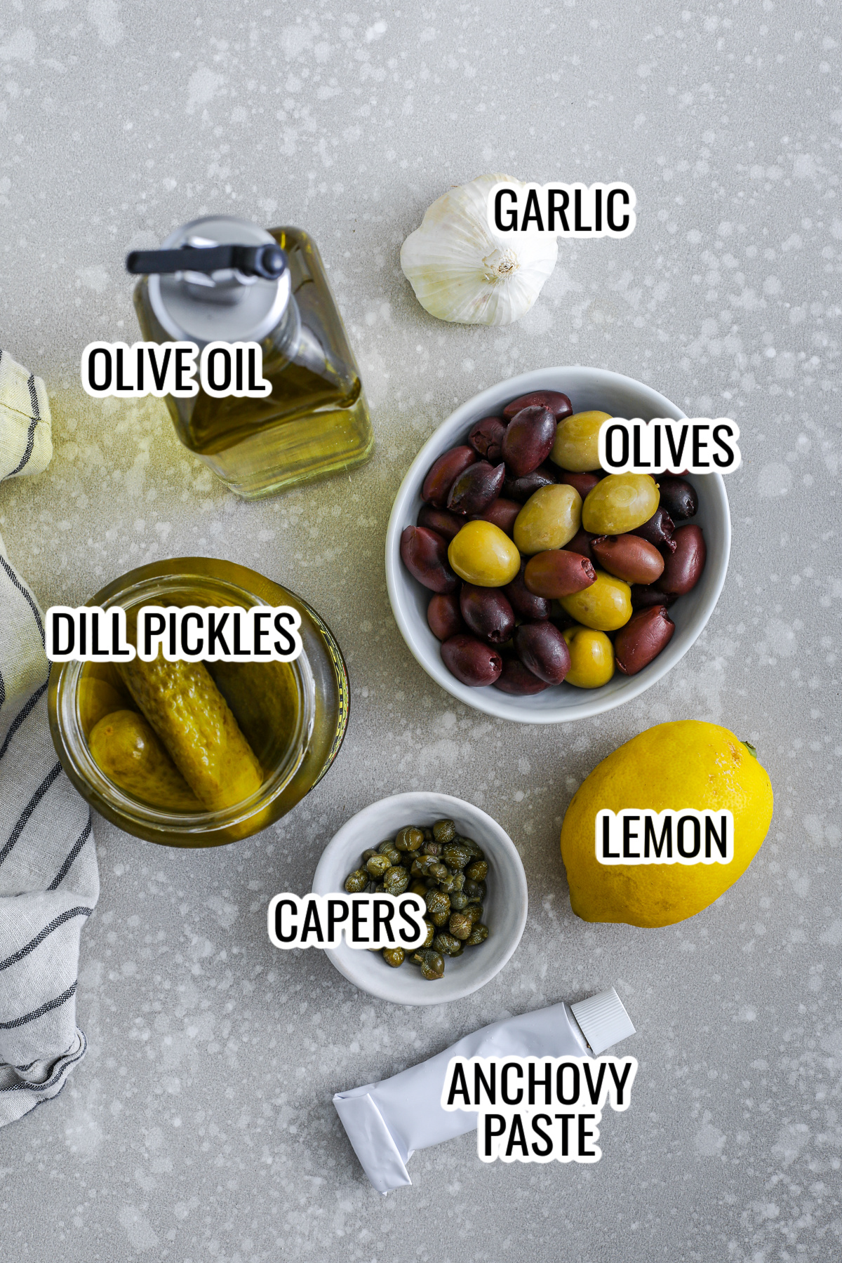 ingredients assembled to make dill pickle tapenade recipe, including olives, dill pickles, olive oil, garlic, capers, anchovy paste, and lemon