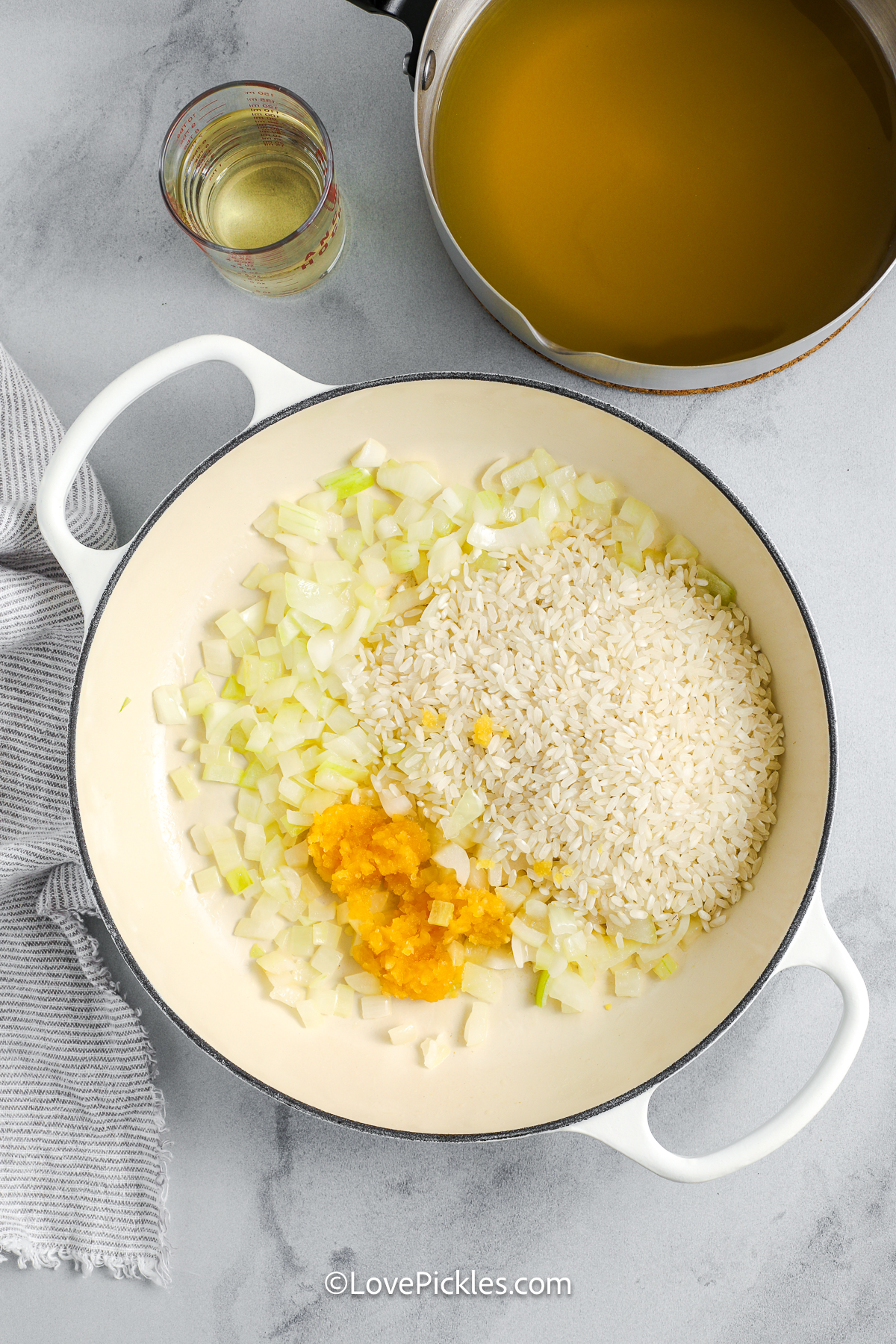 Dill risotto is creamy and bursting with bold dill flavor. Onions and garlic are sautéed first, then arborio rice slowly cooks in warm broth, with a splash of pickle juice adding tang. A little white wine deepens the taste, while butter and Parmesan cheese finish it off creating a silky texture and savory taste. This dish is comforting, bright, and perfect for anyone who loves unique flavors and cozy meals. #lovepickles onion, garlic, and rice in a pot