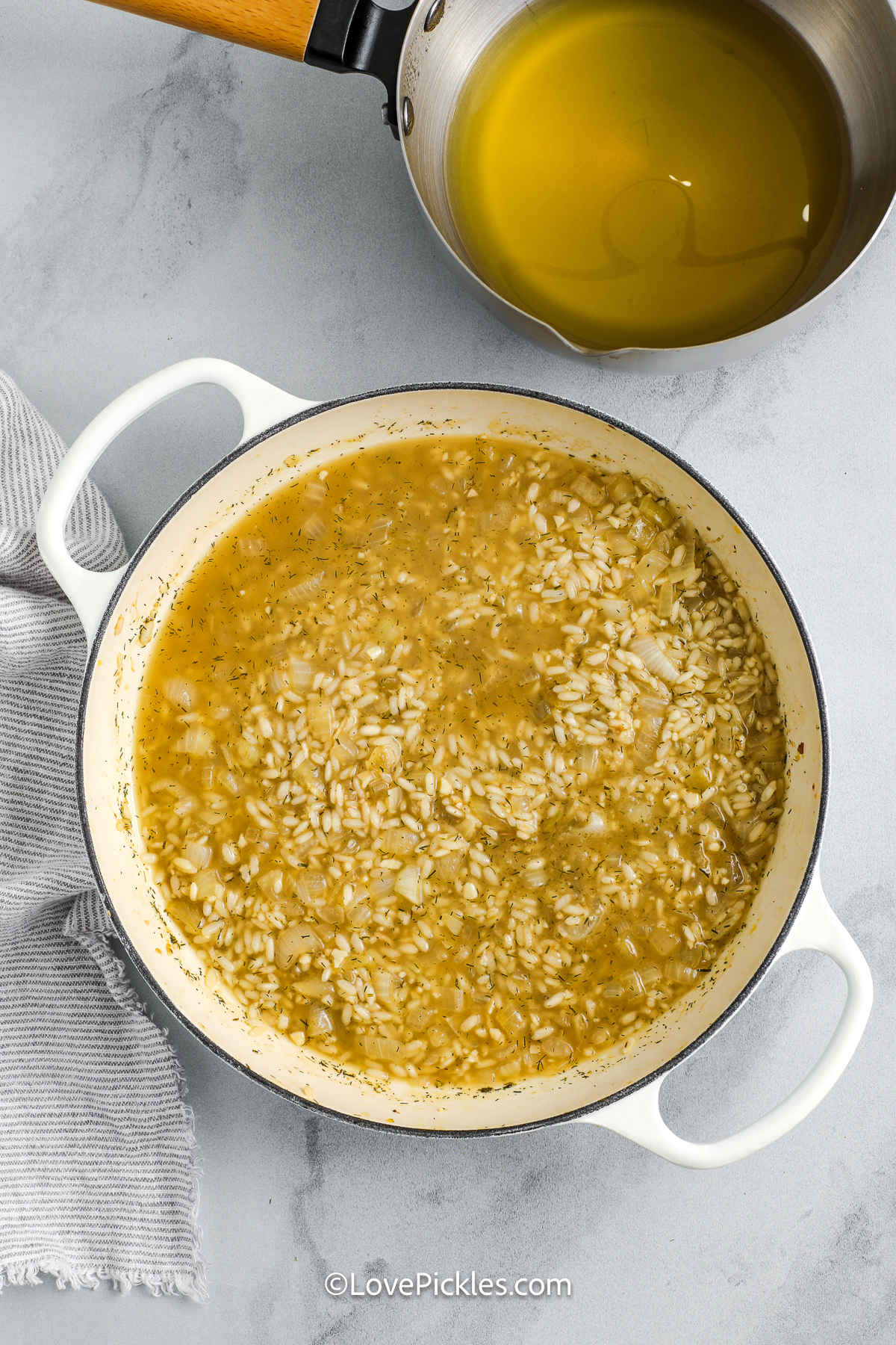Dill risotto is a tangy, herby spin on a classic Italian comfort food. The arborio rice soaks up flavorful broth and pickle juice, building a rich and creamy base. Onions, garlic, and dried dill add savory depth, while butter and Parmesan tie everything together. It’s cozy, flavorful, and a must-try for anyone who enjoys bold, briny flavors in a familiar dish. #lovepickles liquids added to pot to make dill risotto