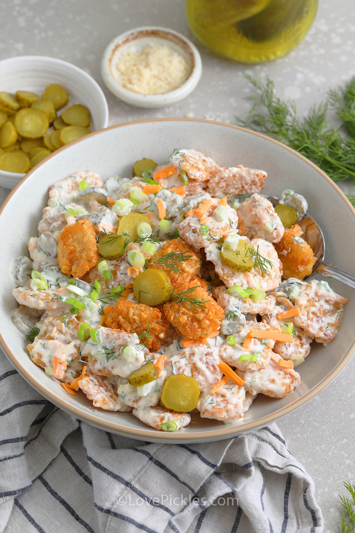 A serving bowl of tater tot pickle salad with a serving spoon