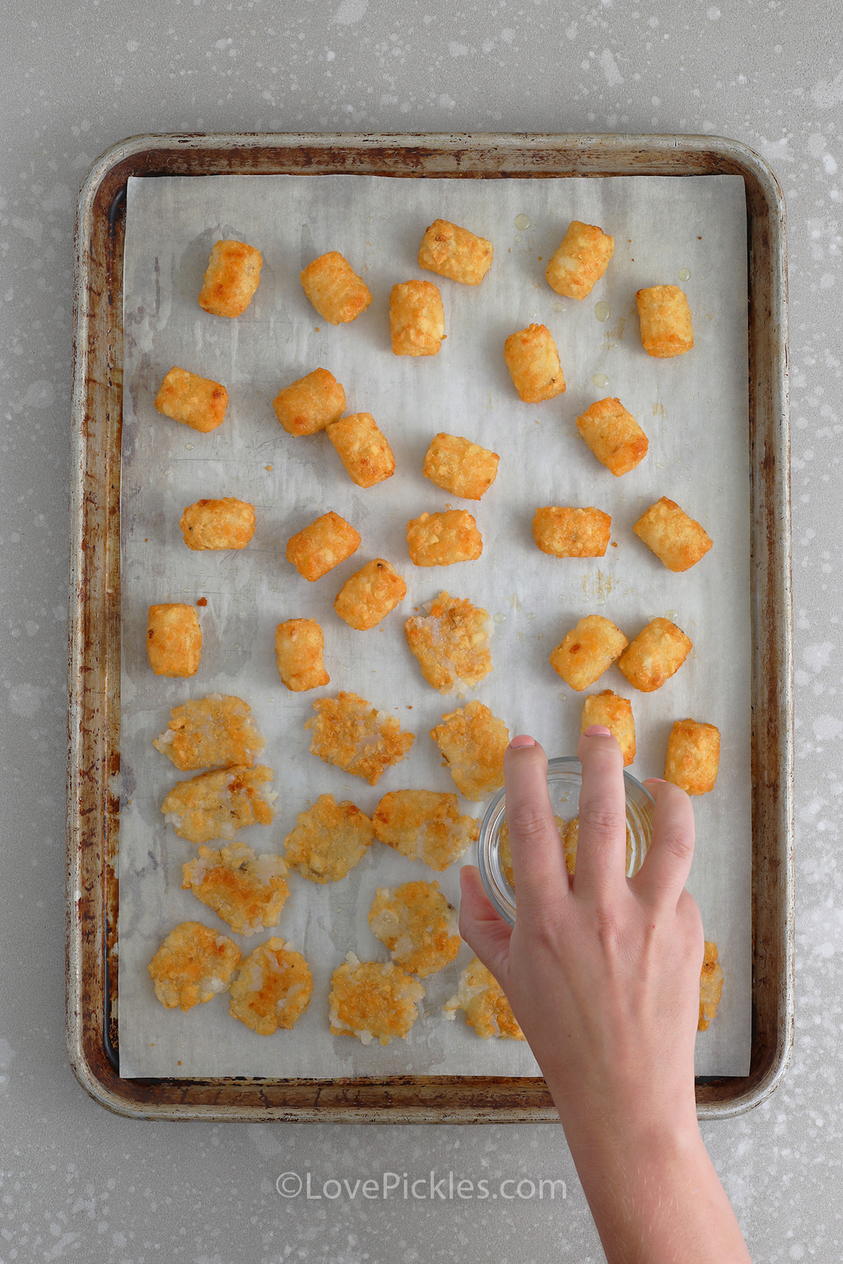 cooked tater tots being squashed on a baking tray to make tater tot pickle salad