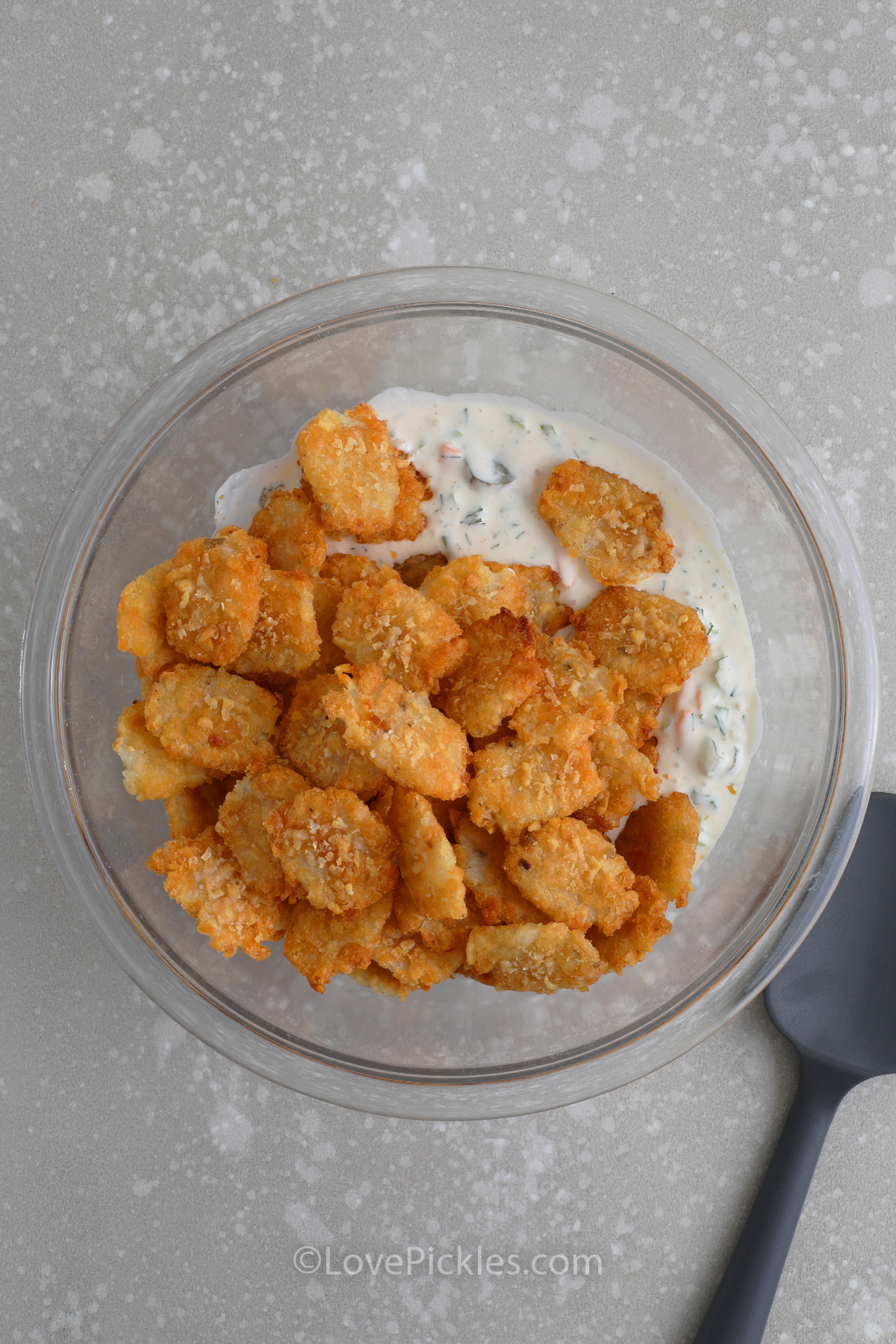 tater tots being tossed with the dressing to make tater tot pickle salad
