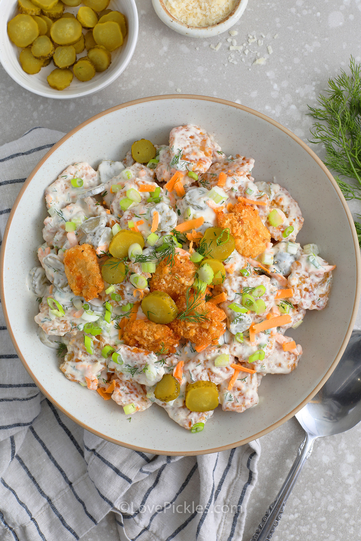 tater tot pickle salad prepared in a bowl topped with smashed tater tots and sliced pickles